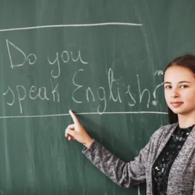 Niña mostrando "Do you speak English?" en la pizarra